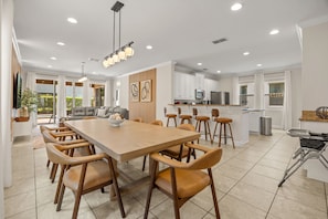 Een moderne keuken met witte kasten, een centraal eiland en een eethoek met een grote houten tafel en stoelen.