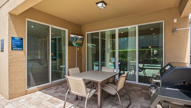 Un patio exterior con mesa y sillas, una parrilla y un puertas correderas que dan a un espacio interior.
