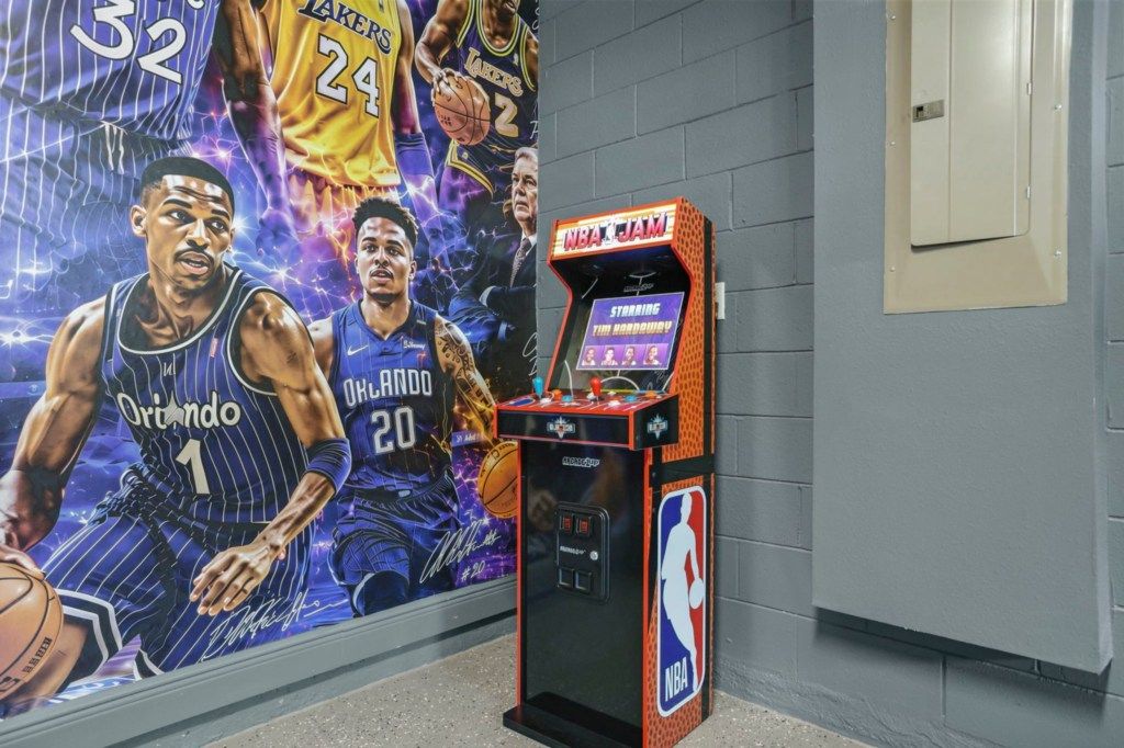 Een basketbal-arcadekast met NBA-branding, voor een muur met een groot poster van basketbalspelers.