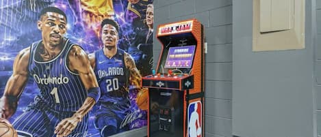 A basketball arcade machine with NBA branding, set against a wall with a large poster of basketball players.