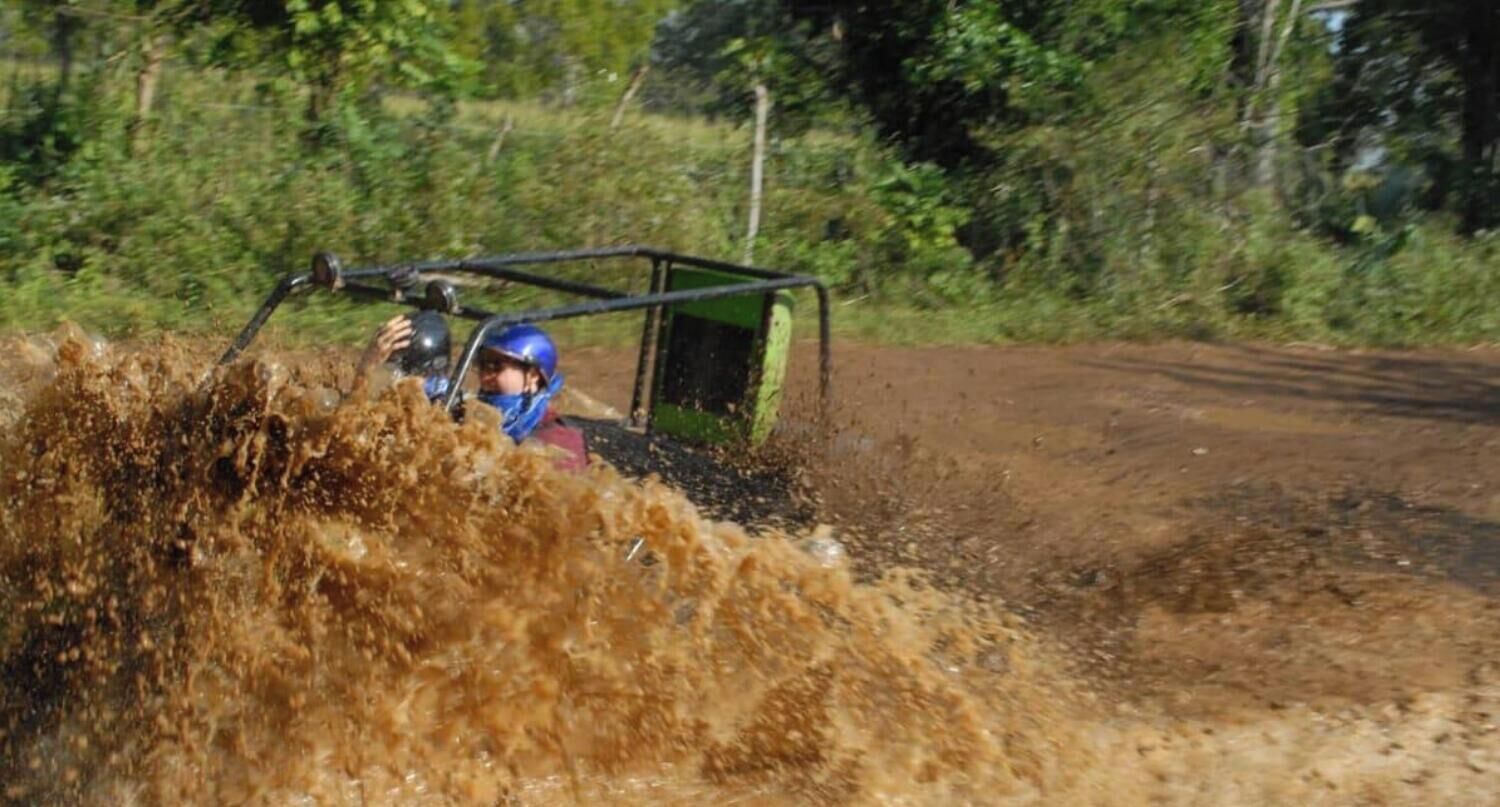 A vehicle navigating a muddy terrain with a person inside wearing a blue helmet.