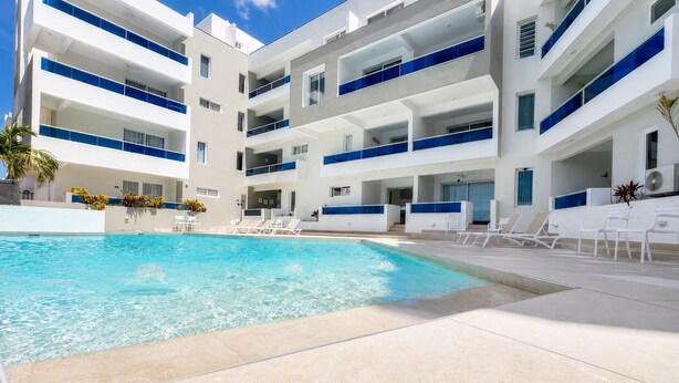 A modern hotel with a swimming pool, multiple balconies, and sun loungers. - ANYA APARTAMENTS (Bayahibe)