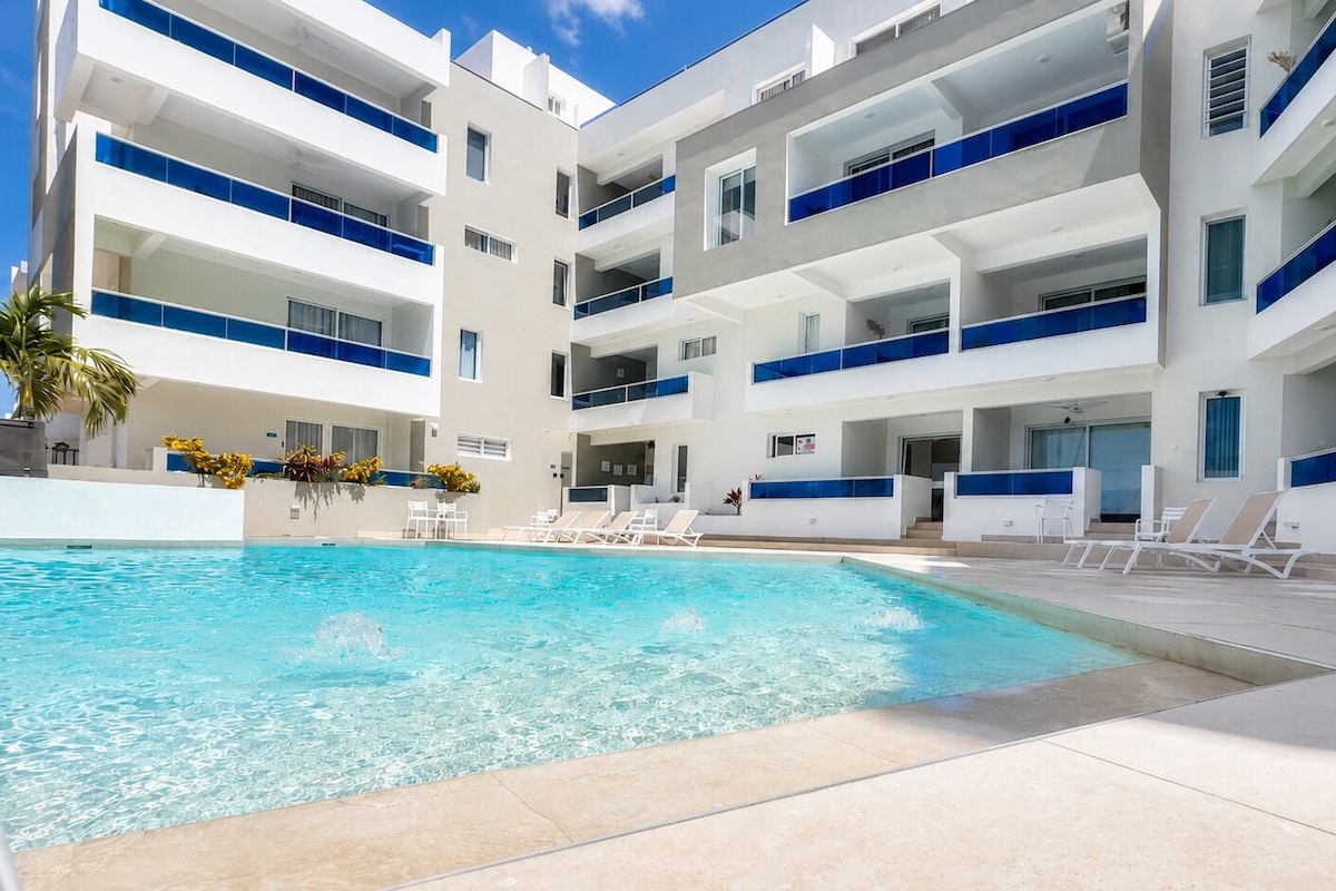 Un hotel moderno con piscina, varios balcones y tumbonas.