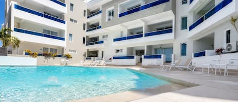 A modern hotel with a swimming pool, multiple balconies, and sun loungers.
