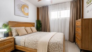 A neatly arranged bedroom with a bed, bedside tables, a dresser, and a window with curtains. - ANYA APARTAMENTS (Bayahibe)