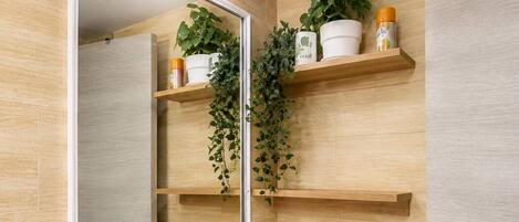 A bathroom with a white sink, a mirror, wooden cabinets, and a shelf with plants and toiletries.