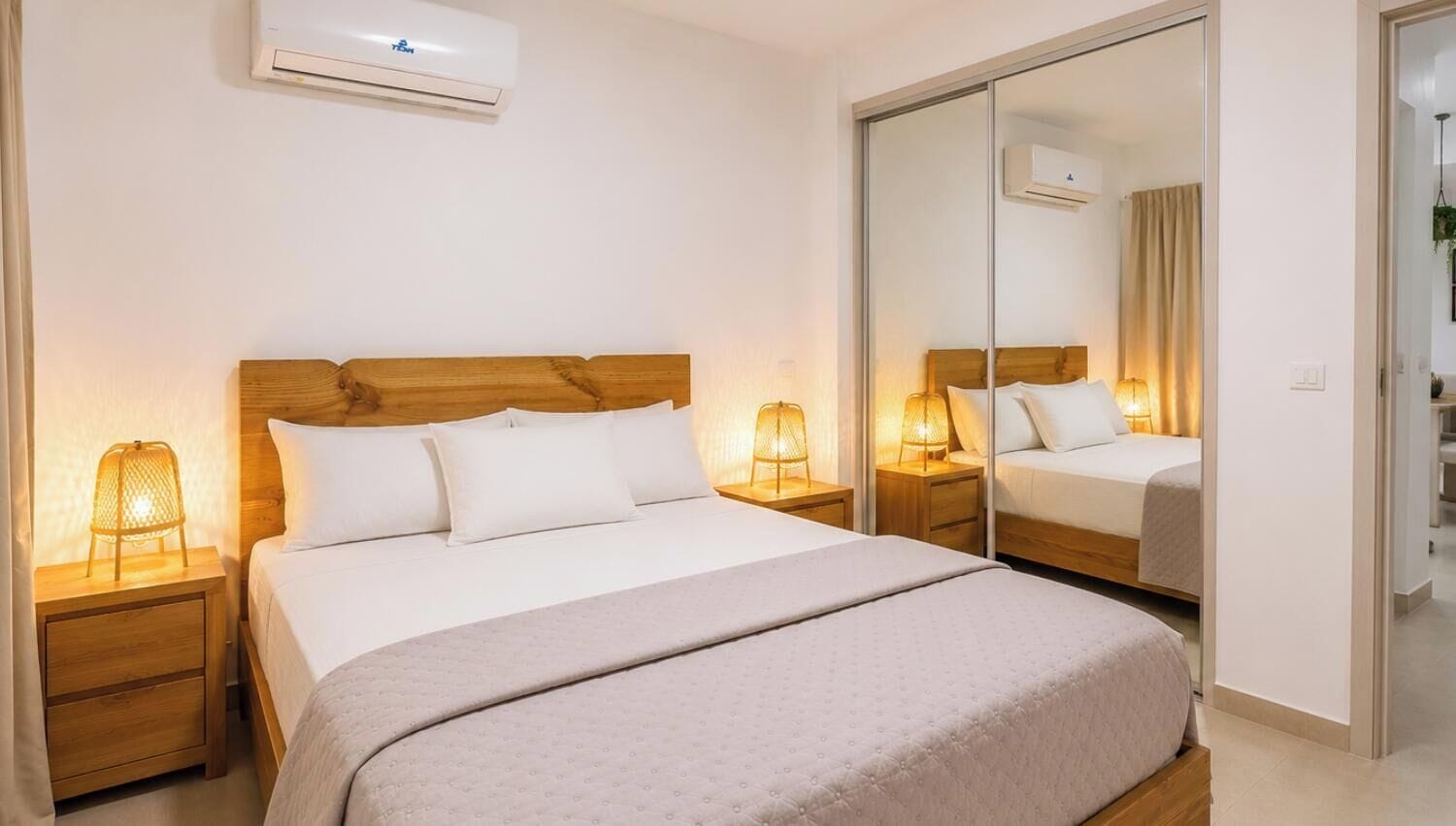 Ein Hotelzimmer mit einem Bett, Nachttischlampen, einem Spiegel und einer Klimaanlage.