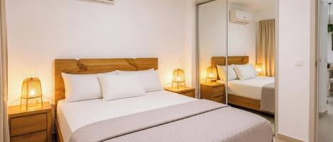 A hotel room with a bed, bedside lamps, a mirror, and an air conditioning unit.