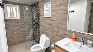 Um banheiro moderno com box de vidro, vaso sanitário branco e toucador de madeira com espelho.