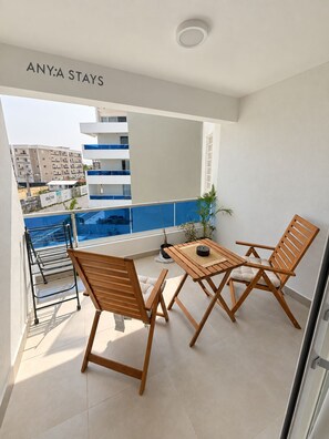 A balcony with a table and chairs, a view of a building, and a sign that reads 'ANYA STAYS'. - ANYA APARTAMENTS (Bayahibe)