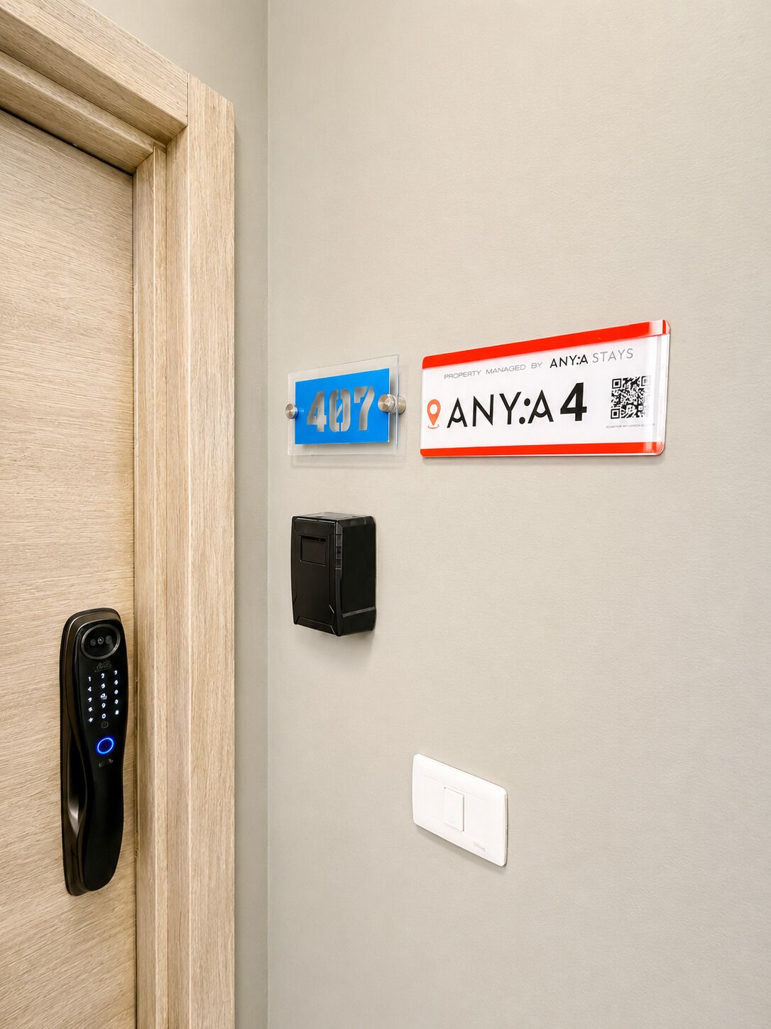 A door with a digital lock, a wall-mounted QR code, a property management sign, and a light switch.