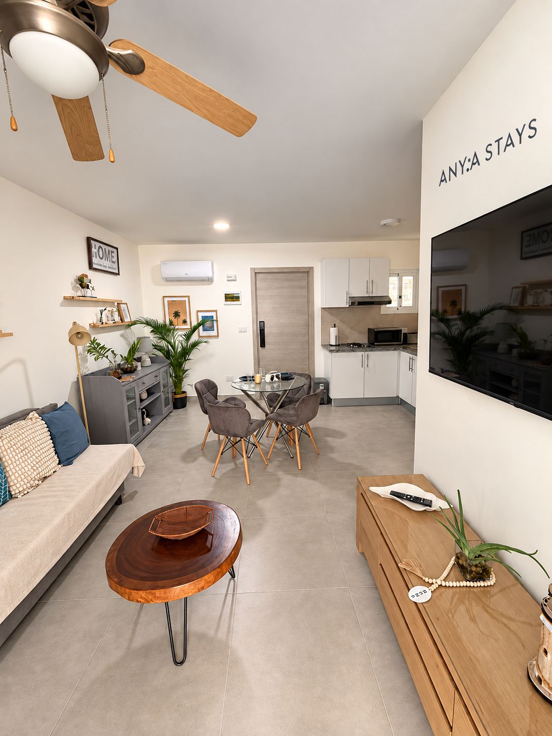 A modern living room with a sofa, coffee table, and dining area. There is a kitchen in the background with cabinets and a microwave.