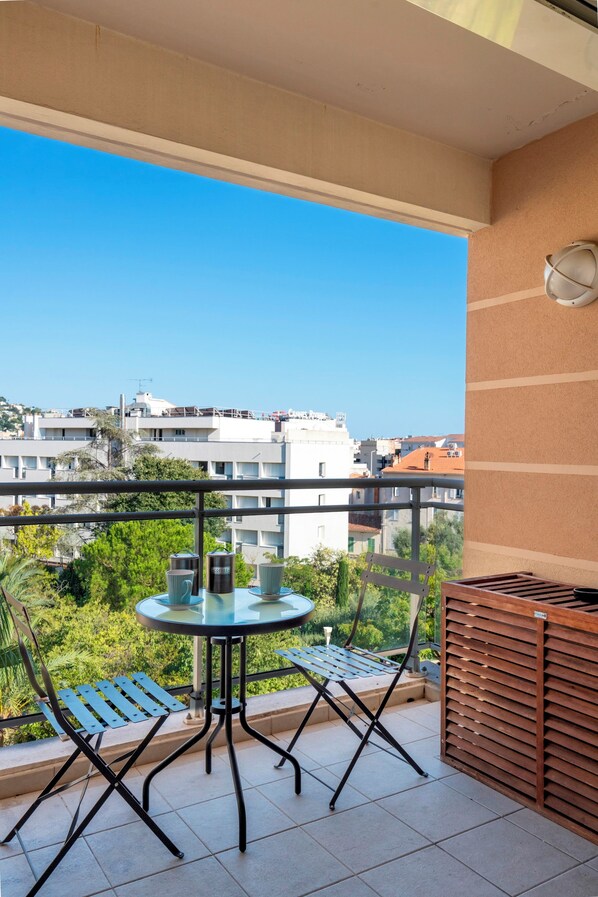 A balcony with a table and chairs, a wooden bench, and a view of the cityscape. - Le Studio du Park avec terrasse et garage (Cannes)