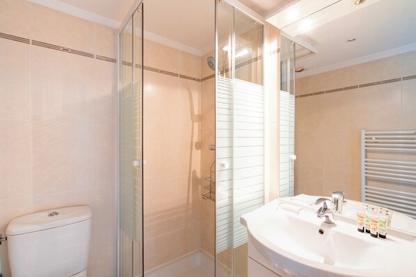 A modern bathroom with a glass shower enclosure, a white toilet, and a sink with toiletries. - Le Studio du Park avec terrasse et garage (Cannes)