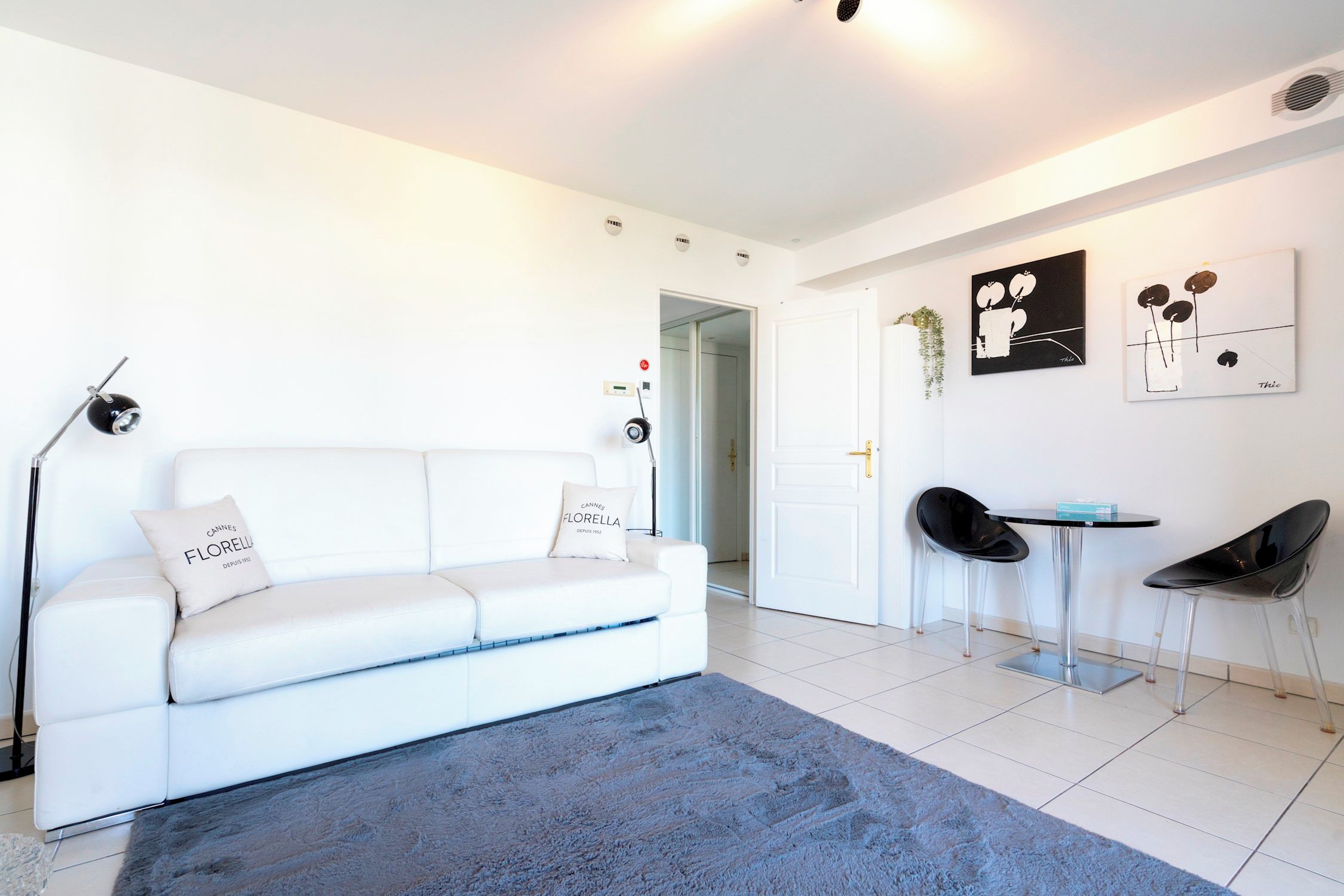 A modern living room with a white sofa, a blue rug, and a dining area with two chairs and a table.