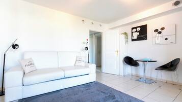 A modern living room with a white sofa, a blue rug, and a dining area with two chairs and a table.