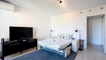 Una camera da letto moderna con una TV a schermo piatto, un letto con biancheria bianca, un tappeto blu scuro e un comodino.