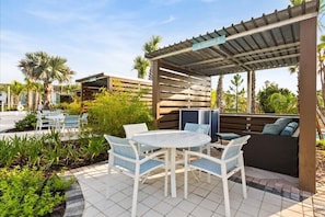 Uma área de estar ao ar livre com um espaço de pátio, uma mesa redonda e cadeiras, um local coberto para sentar e uma piscina ao fundo.