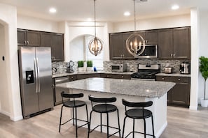 A modern kitchen with a central island, stainless steel appliances, and dark cabinetry. - Spacious 5 Bedroom House close to Strip, Airport, Stadium, Shopping, and Arena (Las Vegas)