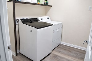 A compact, white front-loading washer and dryer unit in a laundry room with a wooden floor and a beige wall. - Spacious 5 Bedroom House close to Strip, Airport, Stadium, Shopping, and Arena (Las Vegas)