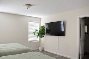 A bedroom with two beds, a television mounted on the wall, a potted plant, and a window with blinds. - Spacious 5 Bedroom House close to Strip, Airport, Stadium, Shopping, and Arena (Las Vegas)