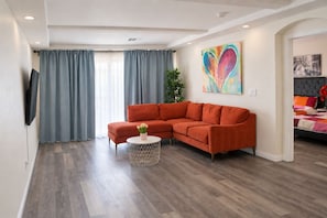 En moderne stue med en hjørnesofa, et rundt sofabord og et stort vindue med gardiner.