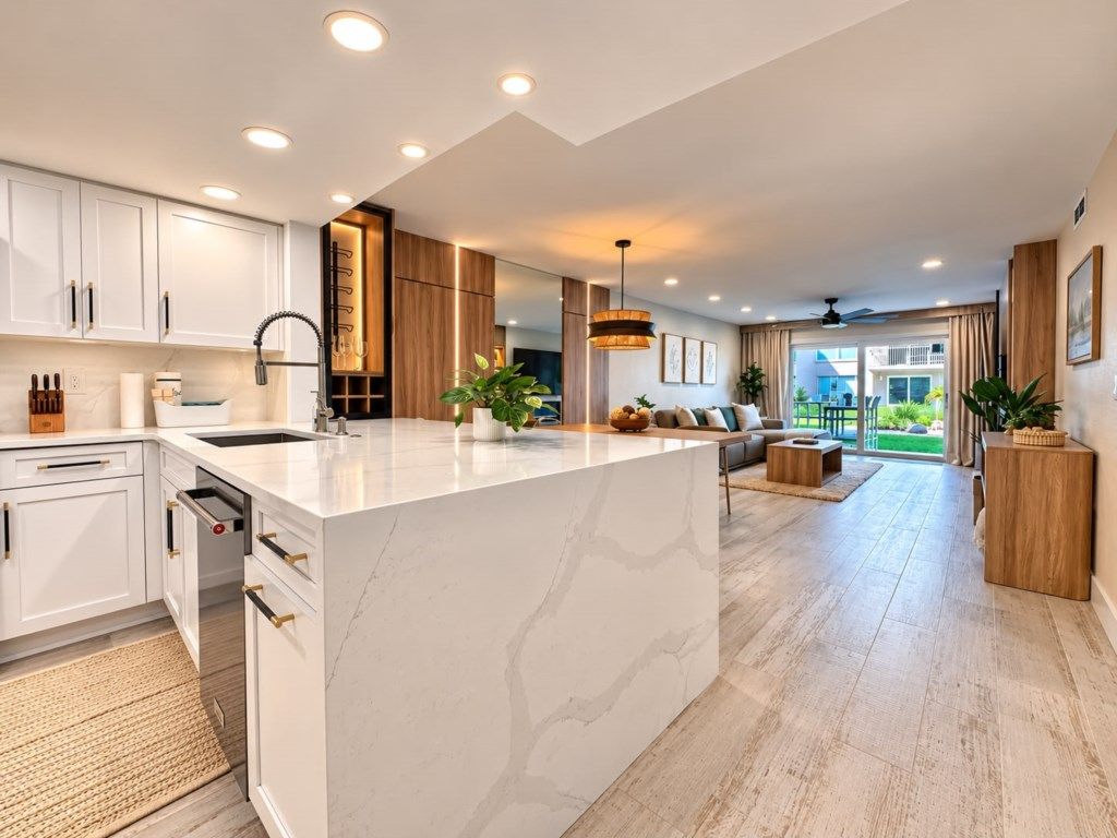 Una cocina moderna con armarios blancos, una isla de mármol y un comedor con sofá y mesa de centro.