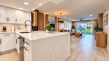 Una cocina moderna con armarios blancos, una isla de mármol y un comedor con sofá y mesa de centro.