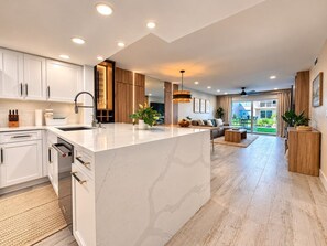 Una cocina moderna con armarios blancos, una isla de mármol y un comedor con sofá y mesa de centro.