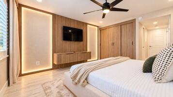 Un dormitorio con cama, ventilador de techo, televisor montado, armarios de madera y una puerta.