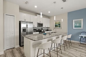 A modern kitchen with white cabinets, stainless steel appliances, a granite countertop, and a bar area with white chairs. - 4 BD/ 3 BA/ Storey Lake (4887 RC) (Kissimmee)