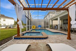 Piscina exterior con una pérgola sobre ella, rodeada de un patio con sillones de descanso.