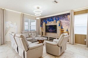 A modern living room with a sectional sofa, a round coffee table, and a large flat-screen TV. - Immersive Experience 9 BD/ 5  BA/ Champions Gate (1513 MC) (Davenport)