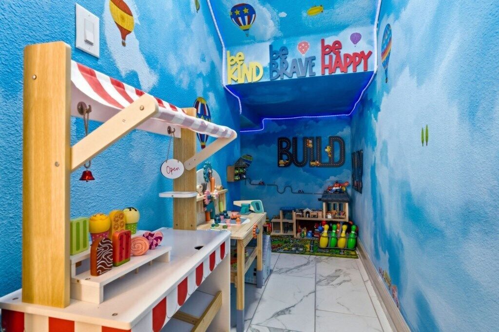 Una sala de juegos con pared azul, una casita de madera y un cartel que dice 'be KIND BRAVE HAPPY'.