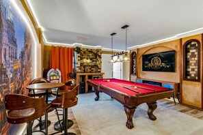 Una mesa de billar en una habitación con un mural, un juke box y una mesa de pool.