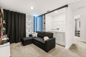 A modern living room with a sectional sofa, a kitchenette, and a laundry area. - 3 BD/ 3 BA/ The Hub at Westside Reserve (3227 SW) (Kissimmee)