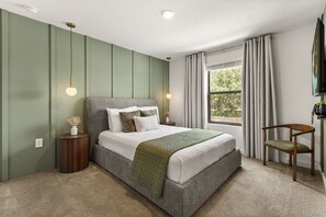Ein Schlafzimmer mit einem Bett, Nachttischen, einem Fenster mit Vorhängen und einem Sessel.