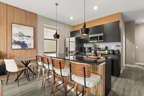A modern kitchen with a central island, bar stools, and a dining area with a table and chairs. - 3 BD/ 3 BA/ The Hub at Westside Reserve (3227 SW) (Kissimmee)
