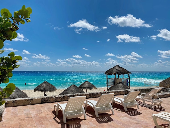 A beach with white lounge chairs and thatched umbrellas, overlooking a clear blue sea.