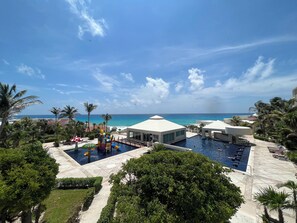 A resort pool area with a view of the ocean, palm trees, and a water slide.