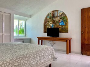 A bedroom with a bed, a TV on a wooden stand, a window, and a door. - Three Bedroom Beachfront Villa (Cancun)