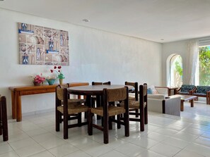 A dining area with a round wooden table and six chairs, a bench, and a wall-mounted shelf with decorative items.