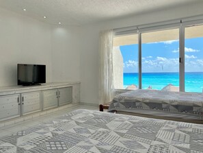 A bedroom with a bed, a TV on a cabinet, and a large window with a view of the ocean.