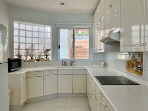 A kitchen with white cabinets, a microwave, a sink, and a window with a view of a brick wall and greenery outside.