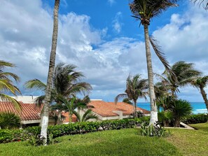 A tropical resort with palm trees, a red-tiled roof, and a view of the ocean. - Three Bedroom Beachfront Villa (Cancun)