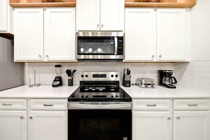A kitchen with white cabinets, a stainless steel microwave, a stove, and a coffee maker. - 7 BD / 5.5 BA / Windsor Cay 1091 OP (Clermont)