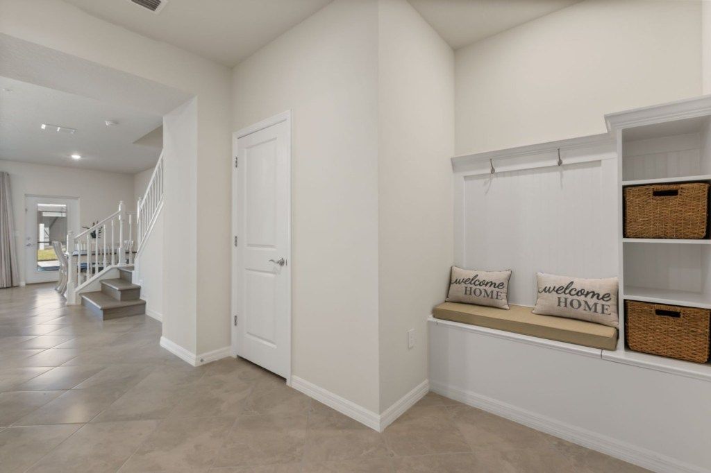 A hallway with a white door, a staircase, and a bench with baskets and pillows.