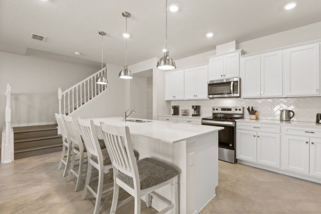 A modern kitchen with white cabinetry, stainless steel appliances, and a central island with bar stools.