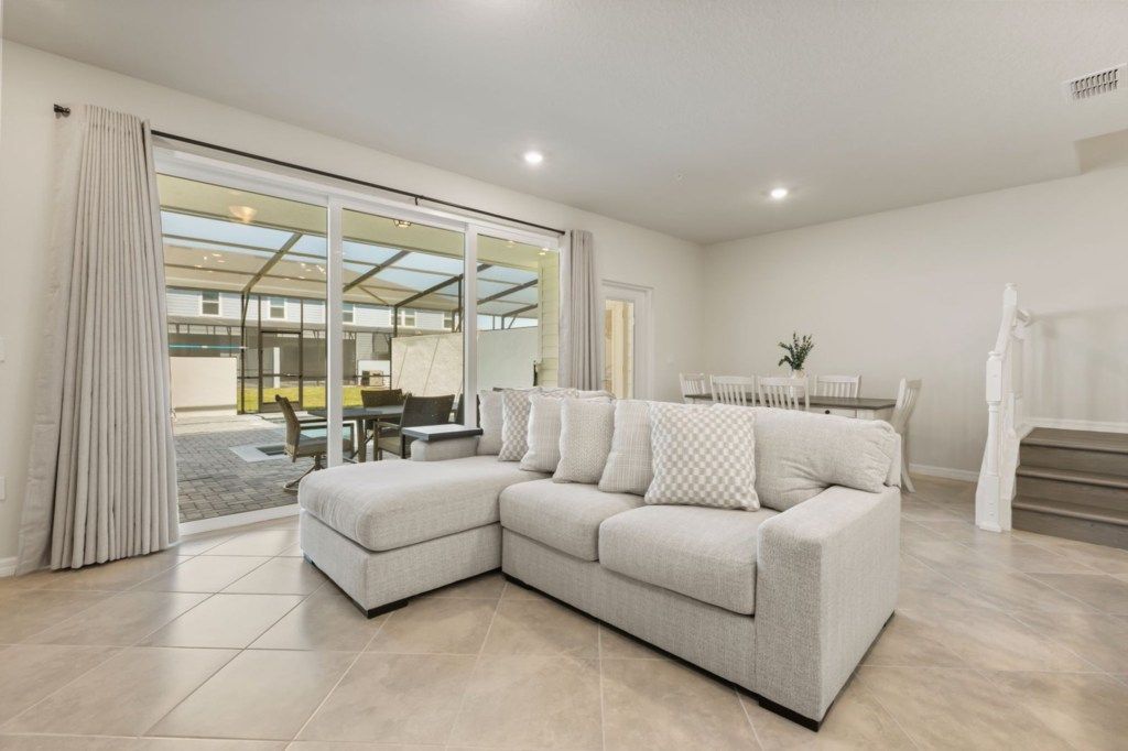 A modern living room with a sectional sofa, a dining area, and a staircase.