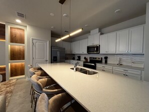A modern kitchen with a large island, white cabinetry, stainless steel appliances, and a bar seating area. - Resort-style 5 BD/ 4.5 BA/ Windsor Cay - 16209 PF (Clermont)